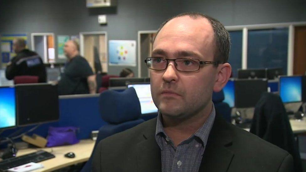 Det Supt Steve Watkins with short dark hair and glasses sitting in a control room