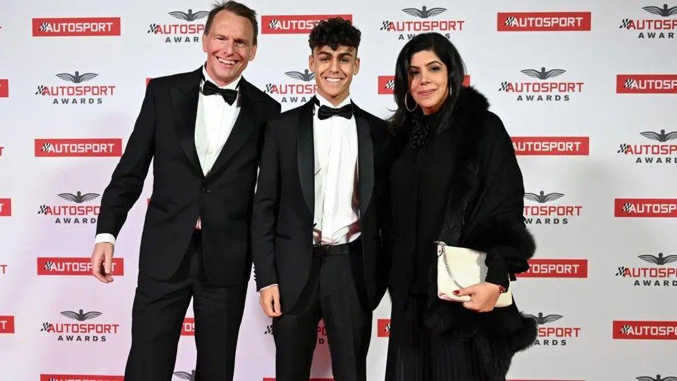 Arvid stands with his dad, Stefan, and his mum, Anita, at the Autosport Awards in 2023. He wears a dark suit and bow die matching his fathers while his mother wears a dark coat trimmed with black fur and carries a white purse. 