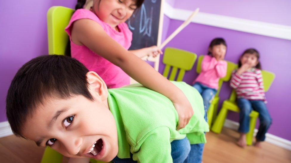 iStock image of children playing in a classroom, one spanking the other with a wooden spoon