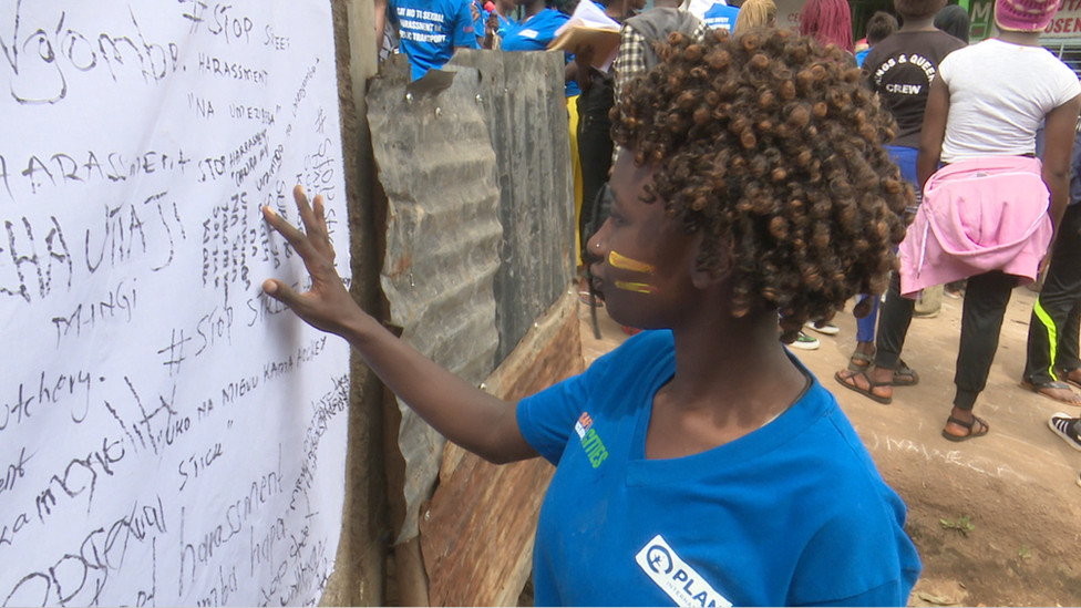 A photo of a young woman in Kibera looking at some of the street harassment messages that were written on canvas by others