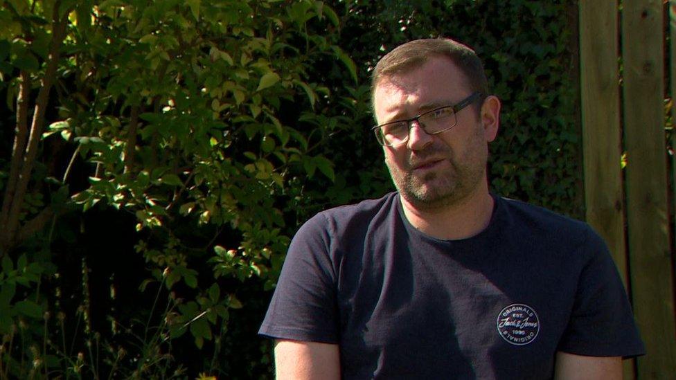 Josh Willis being interviewed outside, sitting in front of some hedges and a fence