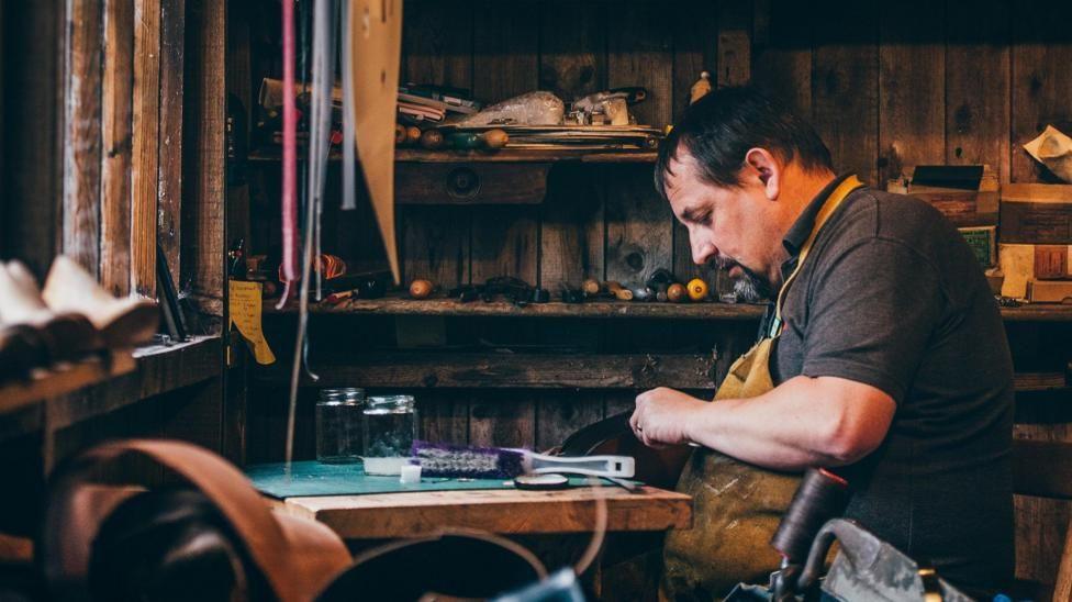 Geraint Parfitt in his workshop. He is sitting in front of a wooden table with a brush on top.