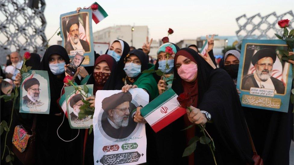 Supporters of Ebrahim Raisi hold up his portrait and roses