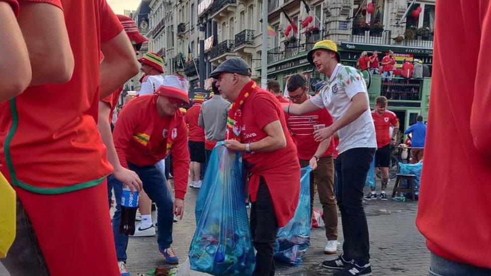 Wales fans carrying blue bags with rubbings and collecting trash on street