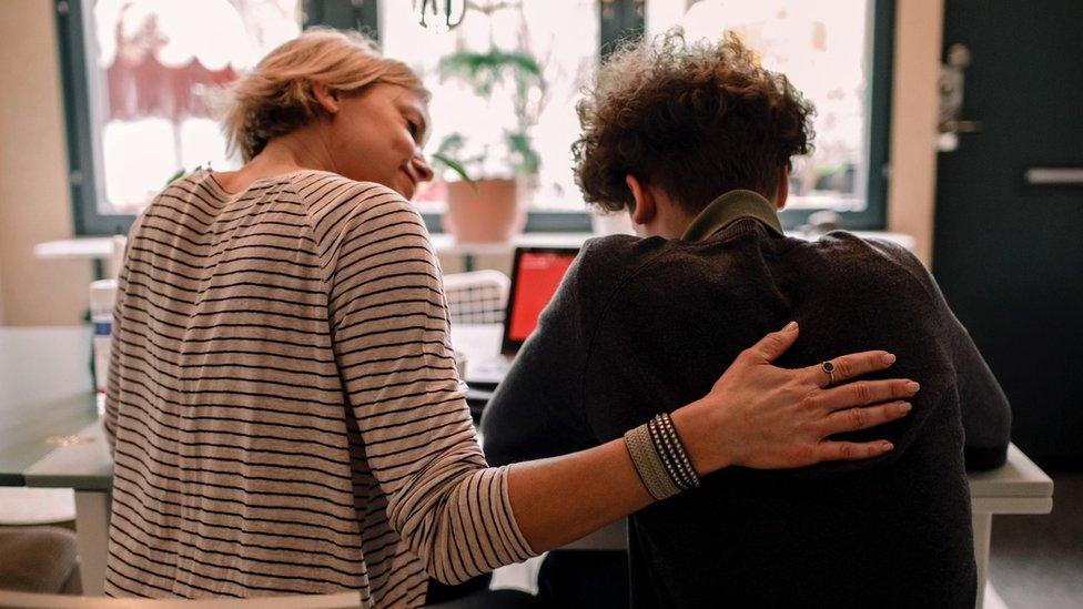 Adult has arm around child comforting them as they do school work