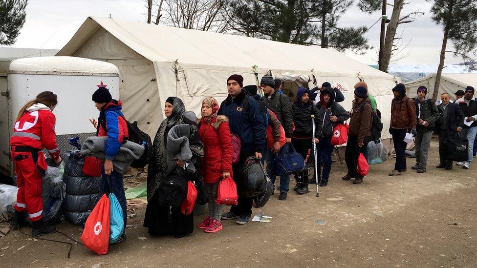 A group of migrants, made up of men and women, queue for aid