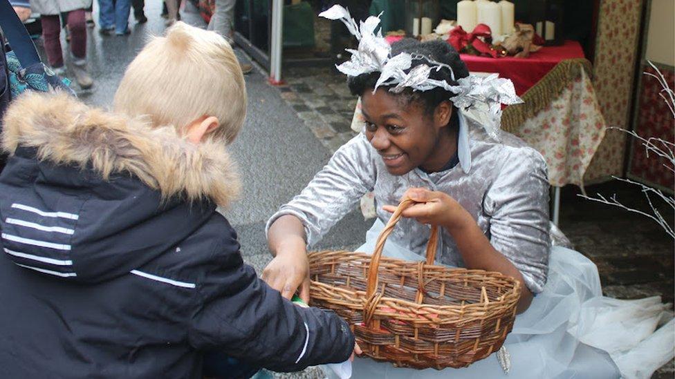 A woman in a white costume with a basket handing a boy something from it