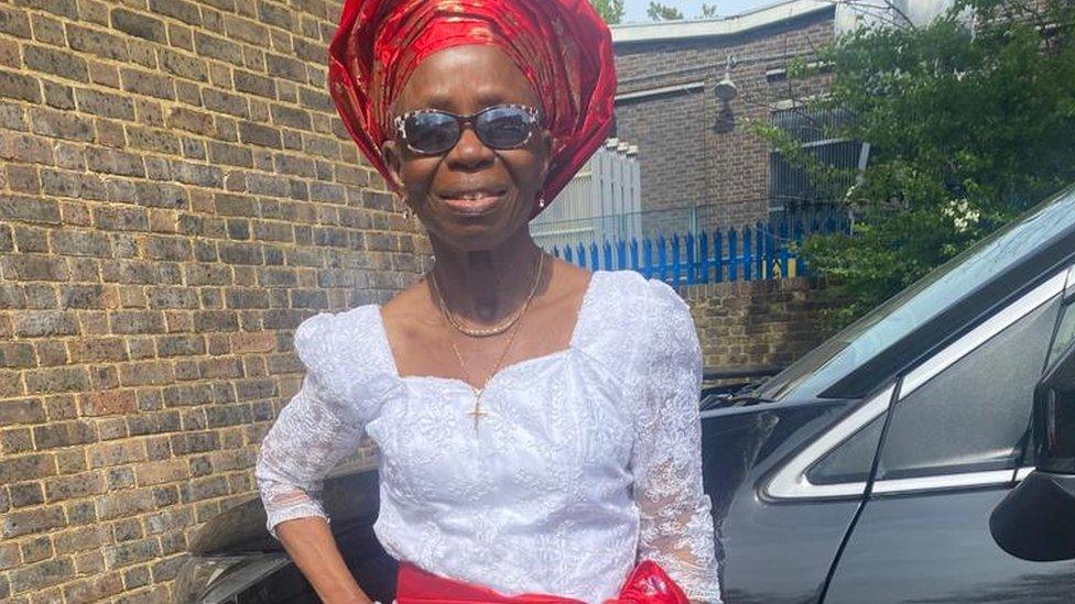 Nelly Akomah, wearing a red headdress, sunglasses and white top.