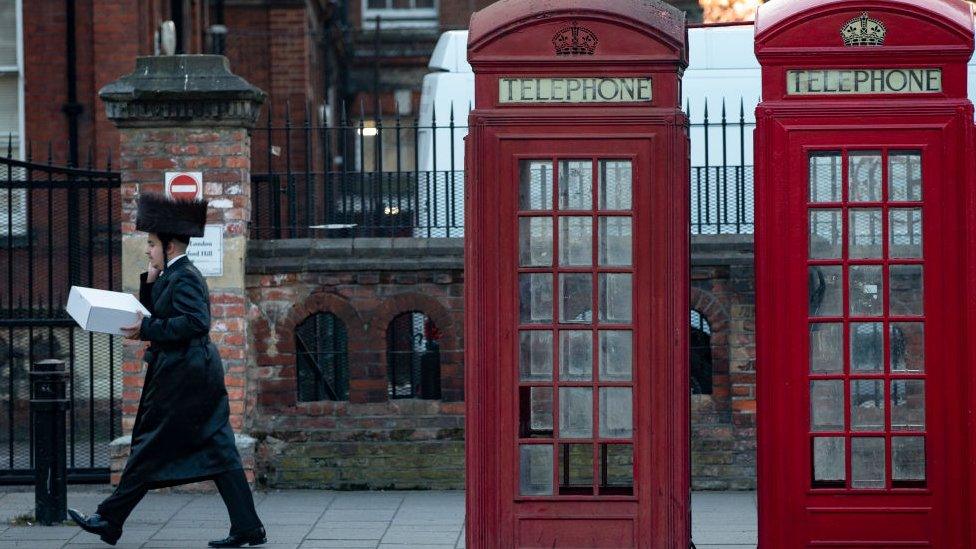 A Jewish man walks past a pair of telephone boxes in Stamford Hill on the evening of the Jewish holiday of Passover on