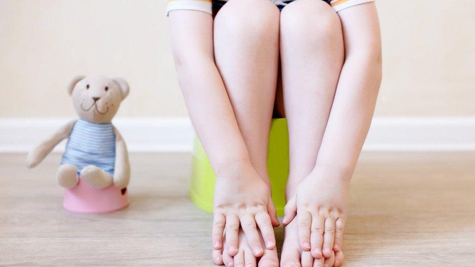 Boy sitting on a potty with his teddy bear next to him