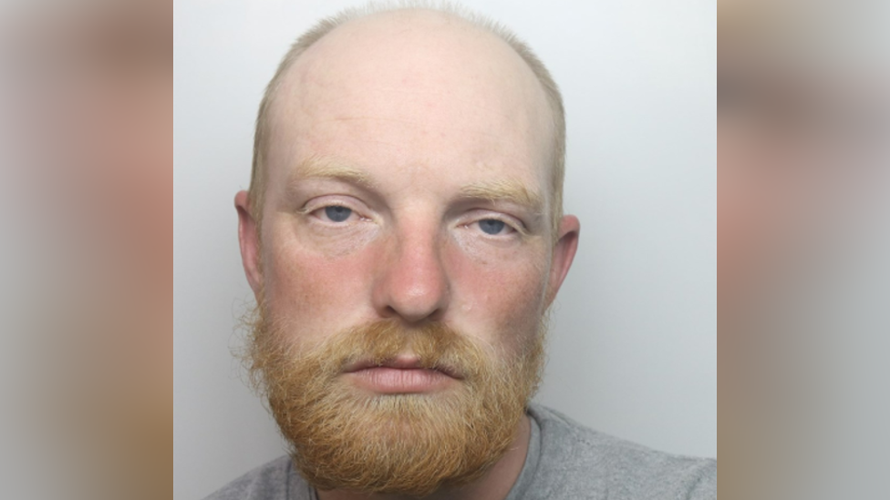 Luke Betts' mugshot. Has thinning, shaved hair and a ginger beard