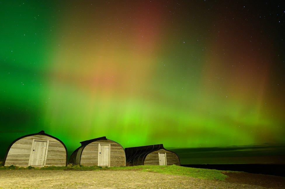 Sheds made from overturned boats with green Northern Lights in the background