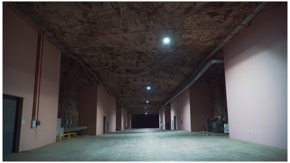 A dark and wide empty hallway underground with storerooms lining the hall