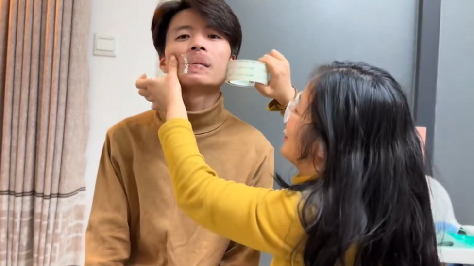 Ms Dong taping her husband's mouth up in a video