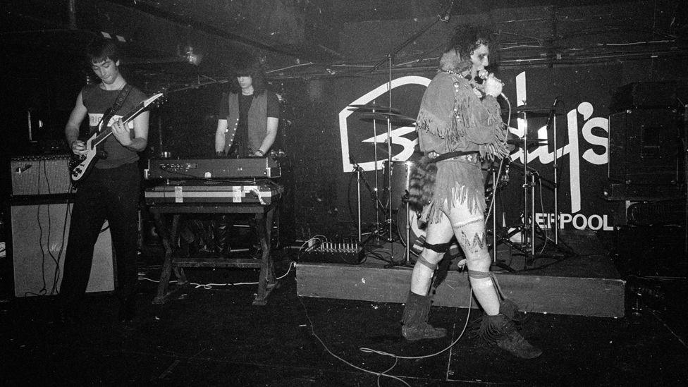 Black and white wide shot of Pere Burns on stage performing with guitarist and keyboard player