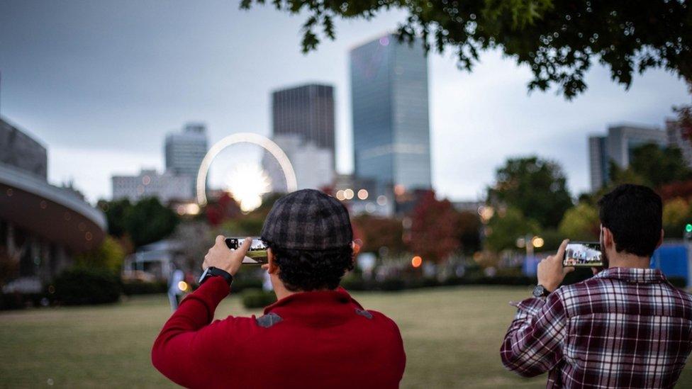 Two people are shown taking photos of Atlanta's skyline.