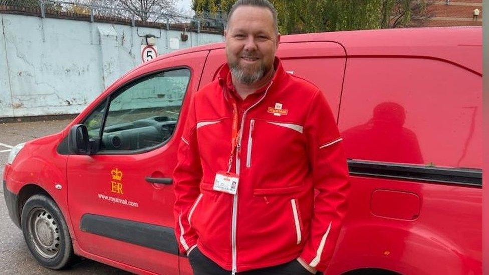 Dan Howells, postman, standing in front of a royal mail van