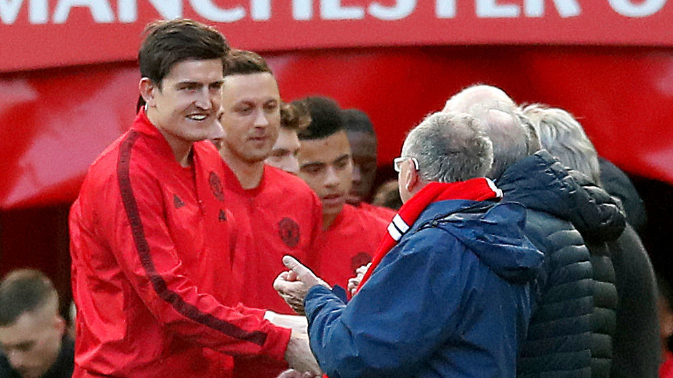 Manchester United's Harry Maguire leads his team out and shakes hands with the "adult mascots" outside the tunnel