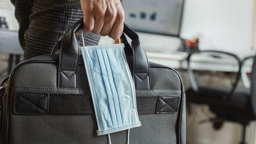 A man carries a laptop bag and a medical mask to work