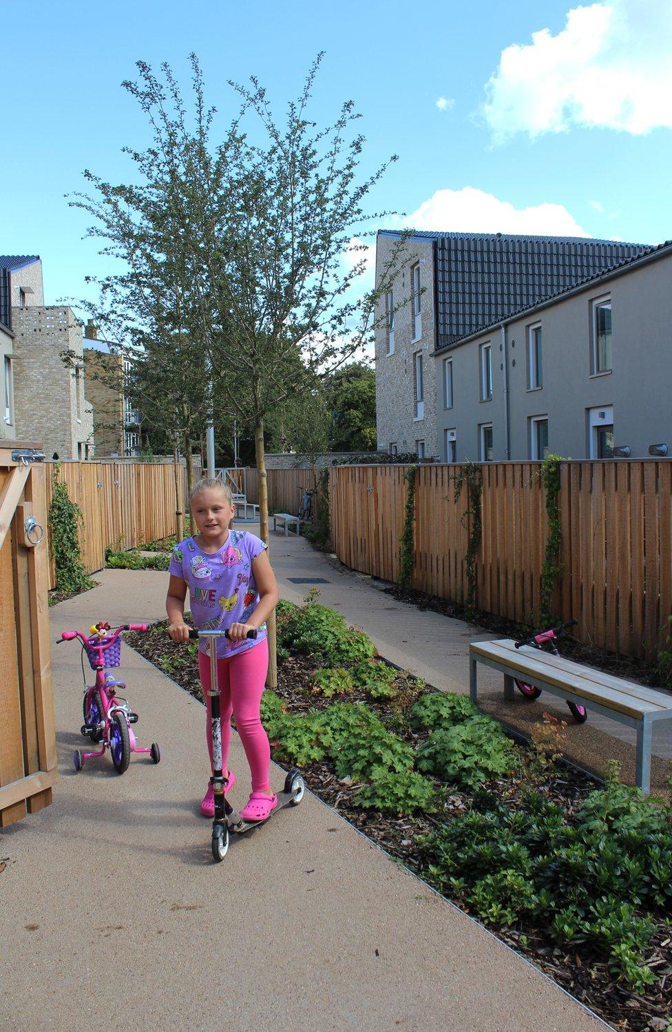 A young girl plays on her scooter in an alleyway