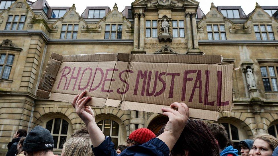 A Rhodes Must Fall campaigner holds up a sign underneath the statue