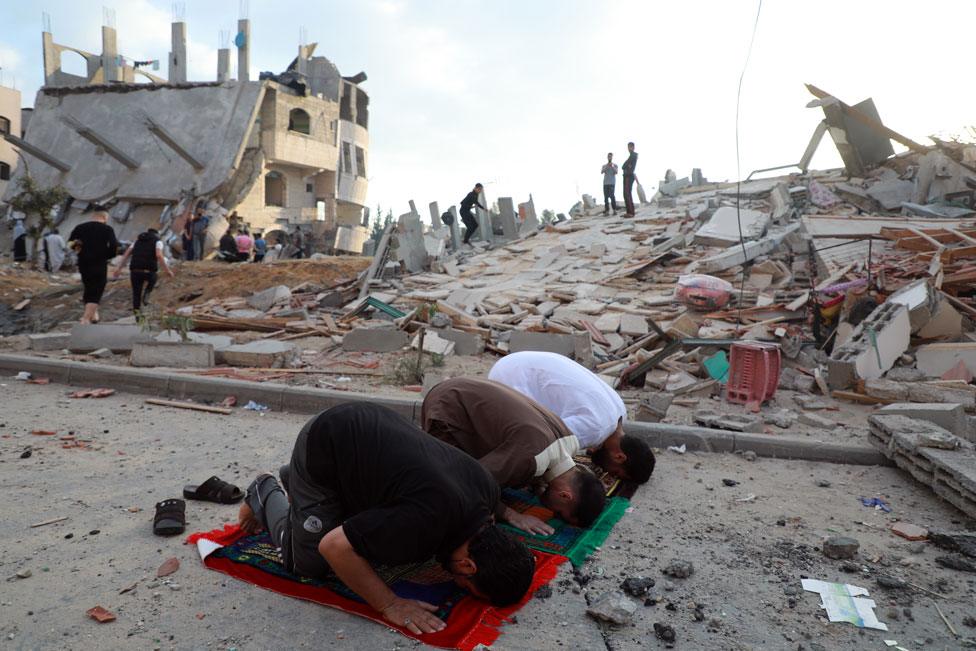 Muslim men perform the morning Eid Al-Fitr prayer with destroyed buildings behind them in Beit Lahia in the northern Gaza Strip