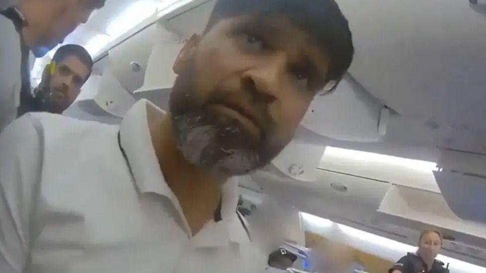 Police footage of Urfan Sharif in a white polo on a plane.