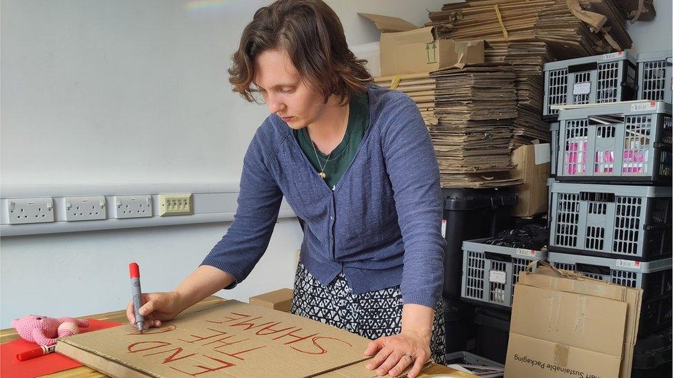 Emily Wilson, CEO of IRise International is making a protest sign which reads 'end the shame'