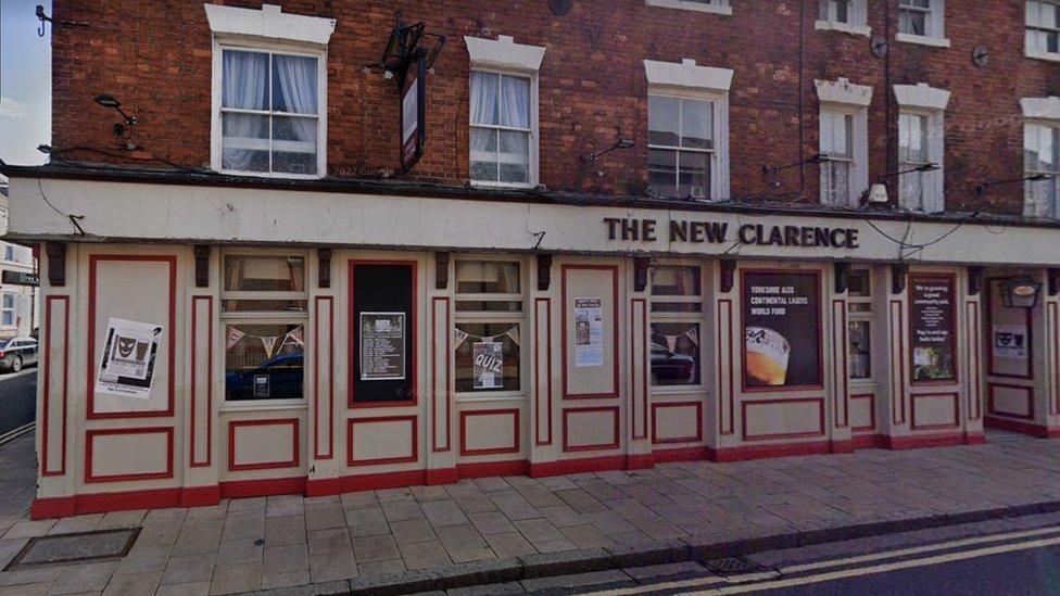 Cream frontage of The New Clarence, with red-lined panels. Above is a redbrick building with a row of six windows.