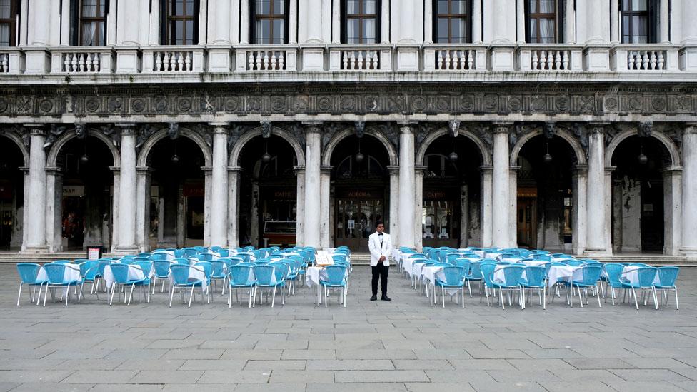 A waiter stands by empty tables outside a restaurant at St Mark"s Square, Venice