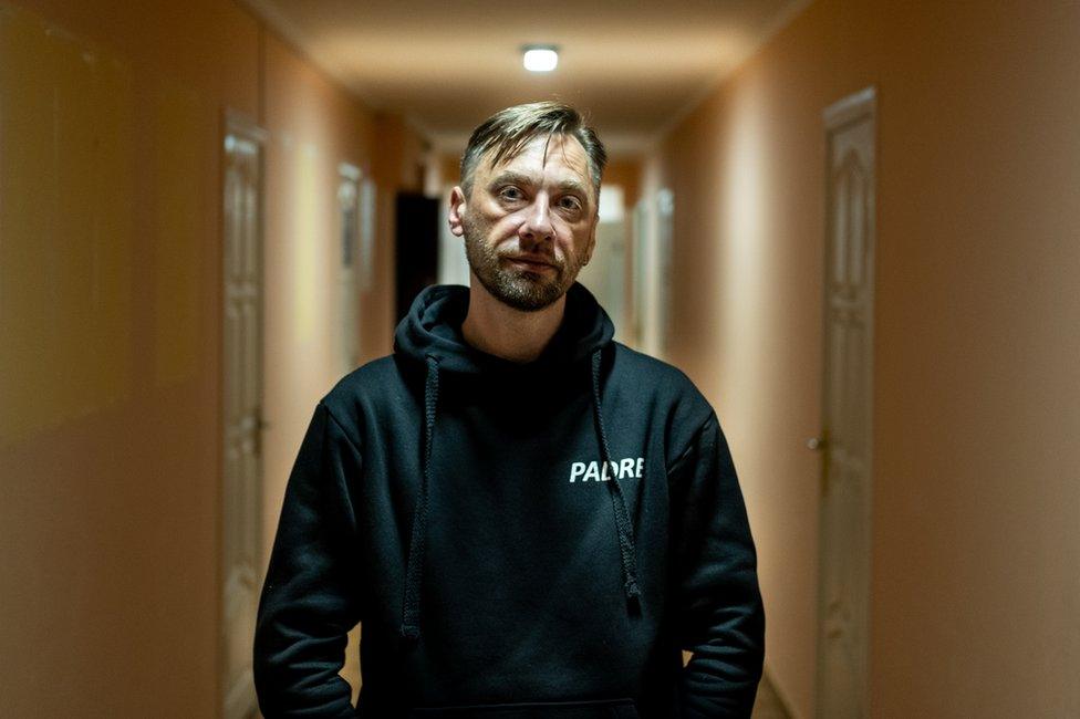 Father Sergey Dmitriev in his office space in Kyiv - wearing black hoodie saying "padre"