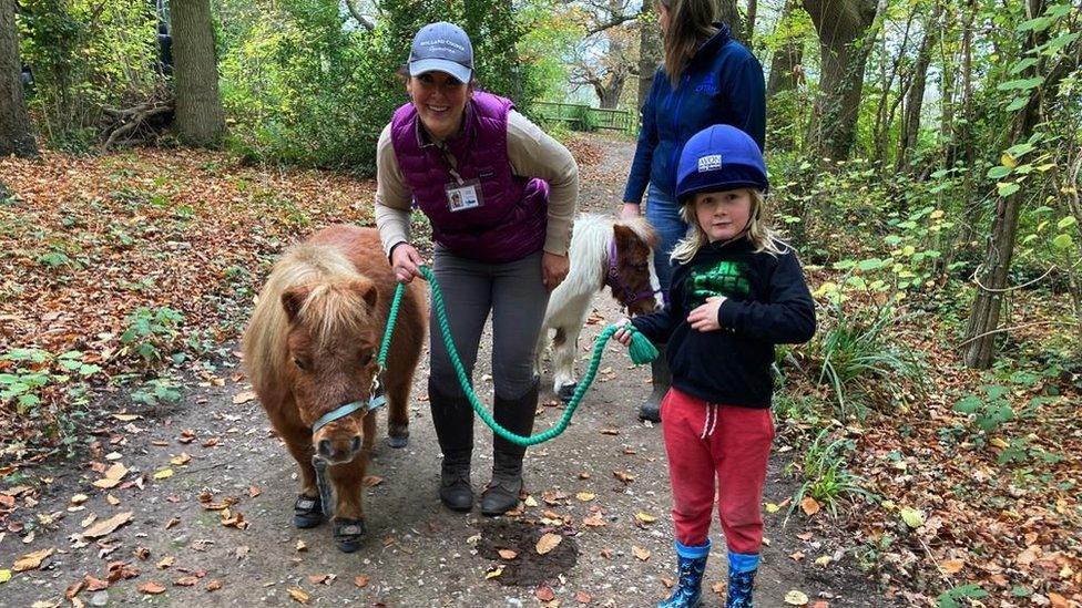 Emma leads a pony on a rein with a child to her left who is walking