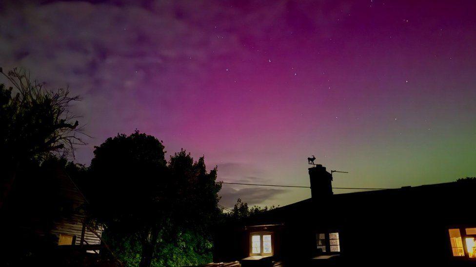 Roof tops and lights seen in windows of homes with green, pink and purple sky