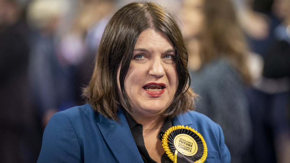 Susan Aitken, with dark hair and a blue jacket and yellow SNP rosette, in a medium close-up 