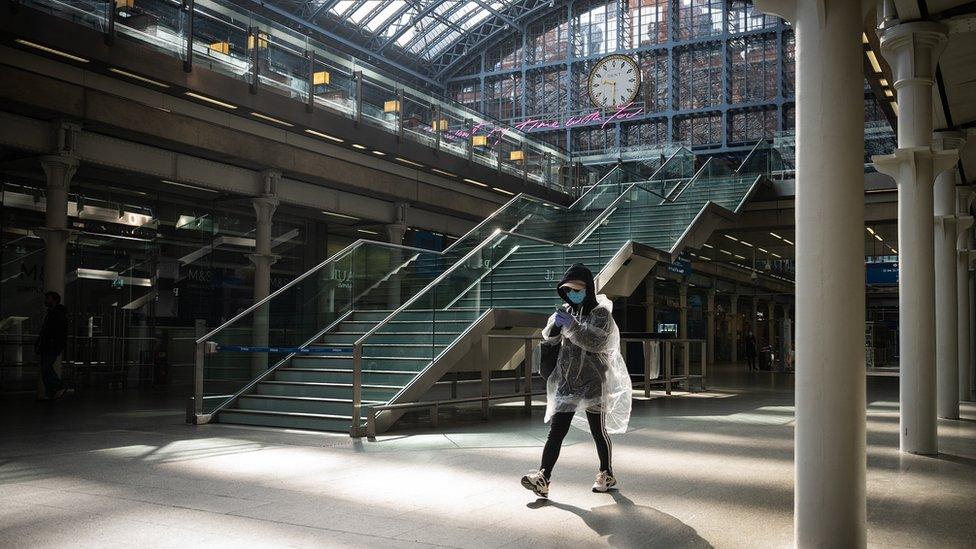 A woman wears a protective mask and plastic raincover as she waits for a train to begin boarding at St Pancras International Station on May 04, 2020 in London, England