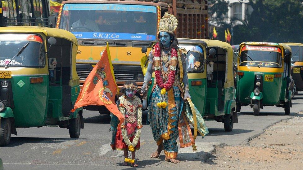 A man dressed as Hindu God Ram walks with his son dressed as monkey god Hanuman