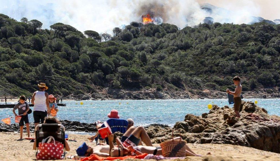 People enjoy the beach during a forest fire in La Croix-Valmer, near Saint-Tropez, on July 25, 2017 as firefighters keep on battling blazes across southern France.