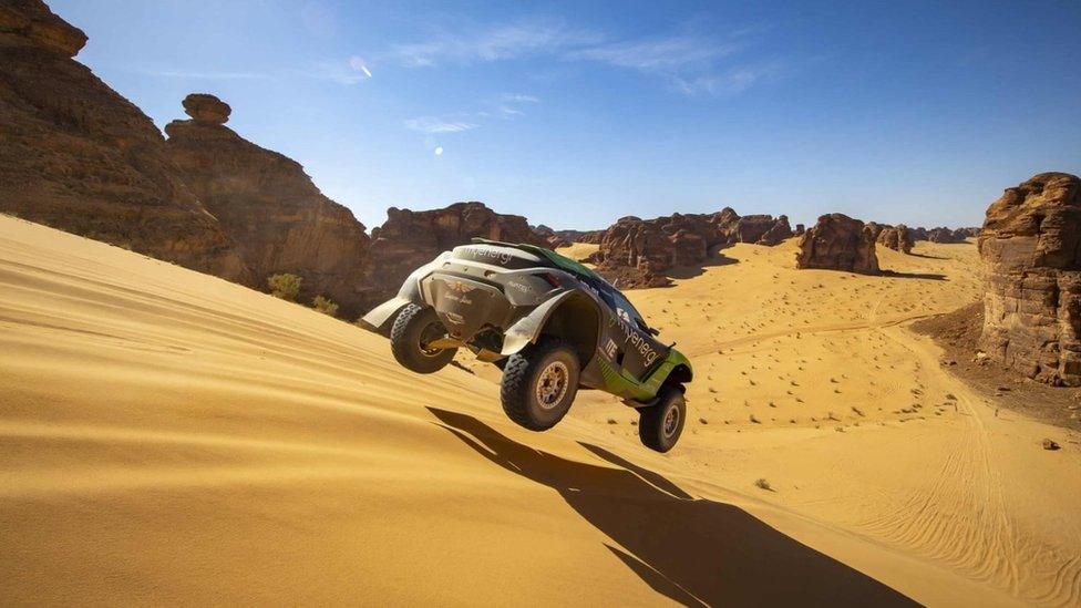 Extreme E SUV with air time as it drives across the sand.