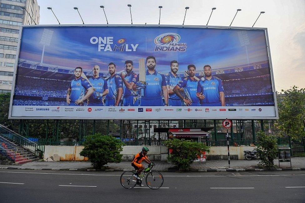 In this picture taken on October 10, 2020, a cyclist rides past a hoarding of Mumbai Indians cricketers of the Indian Premier League (IPL) cricket tournament in Mumbai.