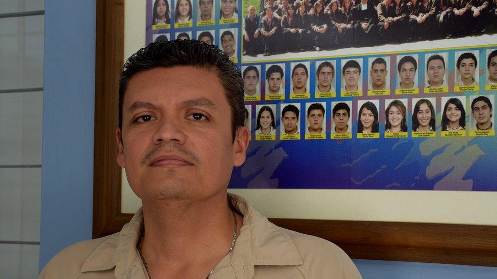 Javier Ramírez in front of a framed photo showing school graduates