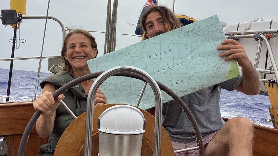 Mr Brady sitting on a sailing boat holding a map that shows the North Atlantic Ocean