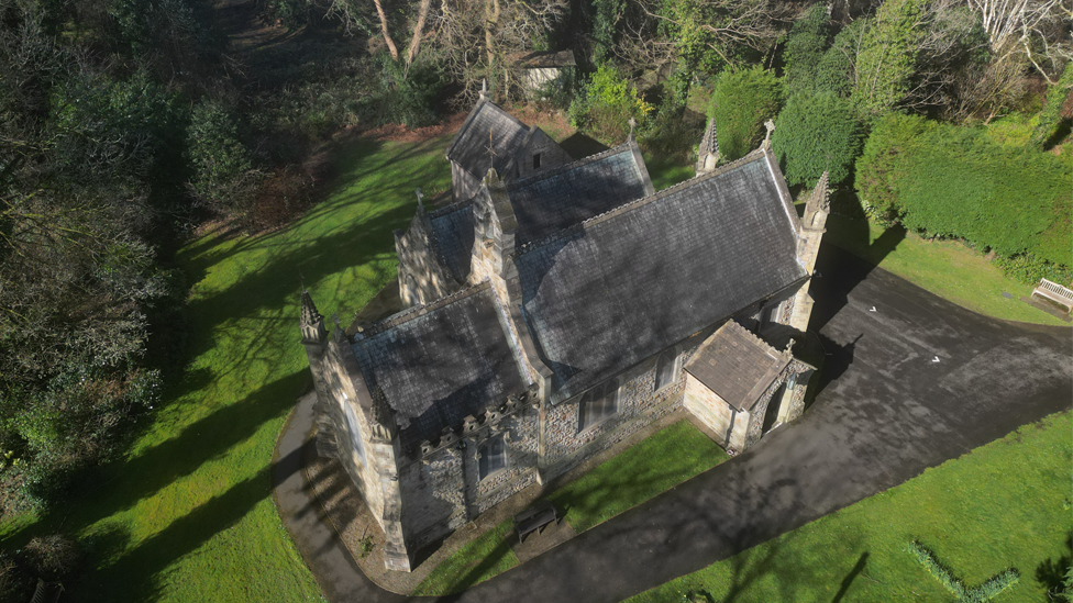 Clyne Chapel, a grey stone church building with a slate roof from above, with grass and trees around it