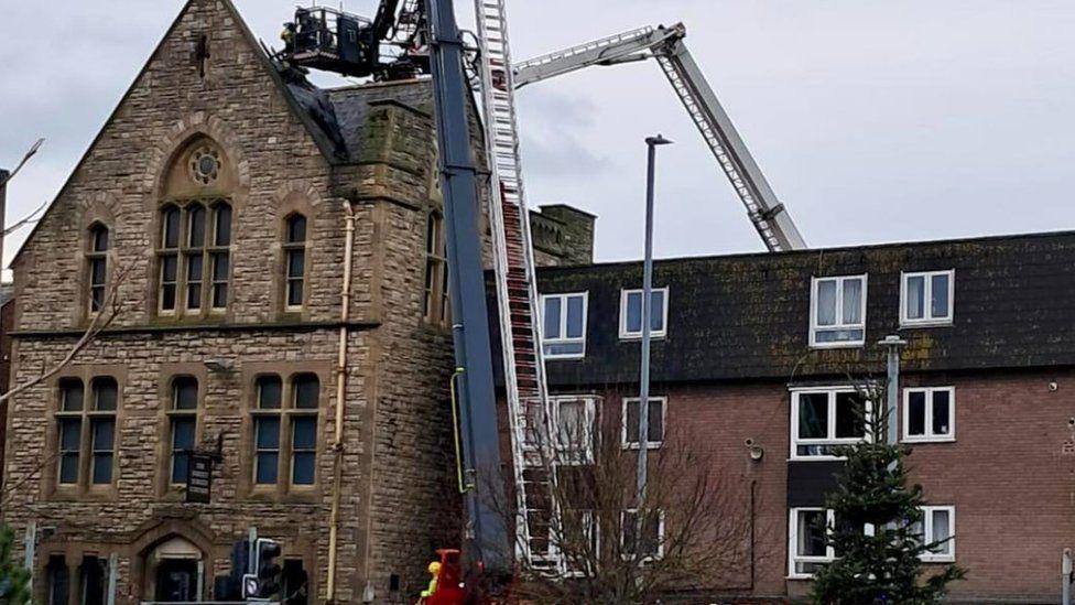 Firefighters on a aerial ladder going up to the roof of a three-storey building 