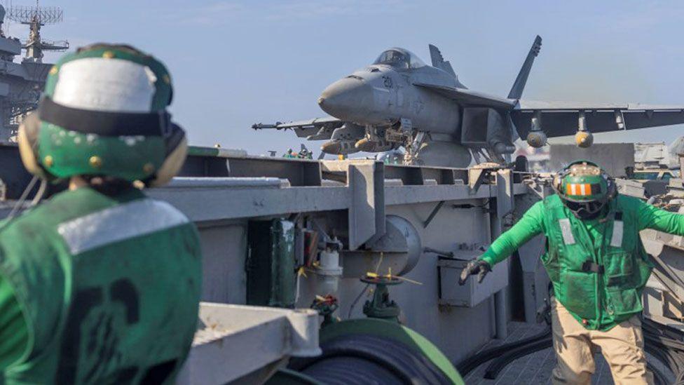 Two men in bright green jackets and helmets can been see in with a US army jet behind them - image released by US Africa Command, February 2025