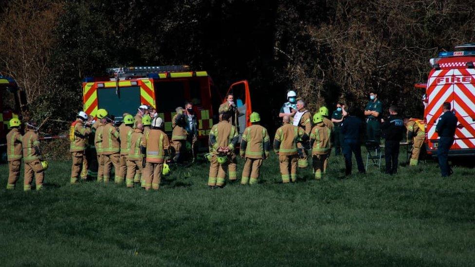 Firefighters at scene by cordon near woods