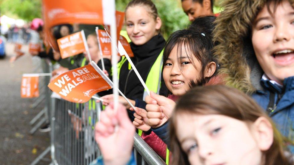 School children line the streets to welcome riders