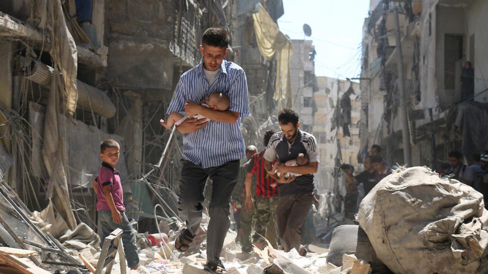 Syrian men carrying babies make their way through the rubble of destroyed buildings following a reported air strike on the rebel-held Salihin neighbourhood of the northern city of Aleppo, on September 11, 2016.