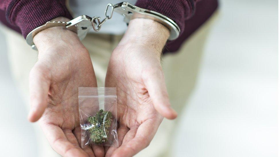 A man in handcuffs holding a bag of drugs