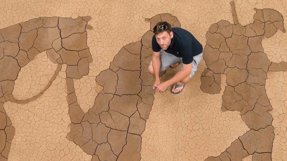 Artist Dan Metcalfe kneeling above his mud memorial installation