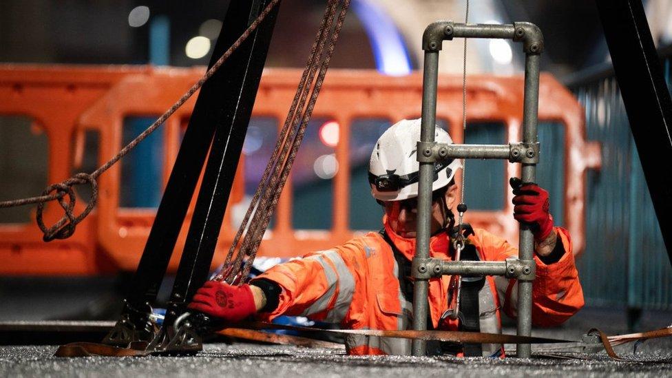 An engineer in orange overalls and a white hardhat descends down a special ladder